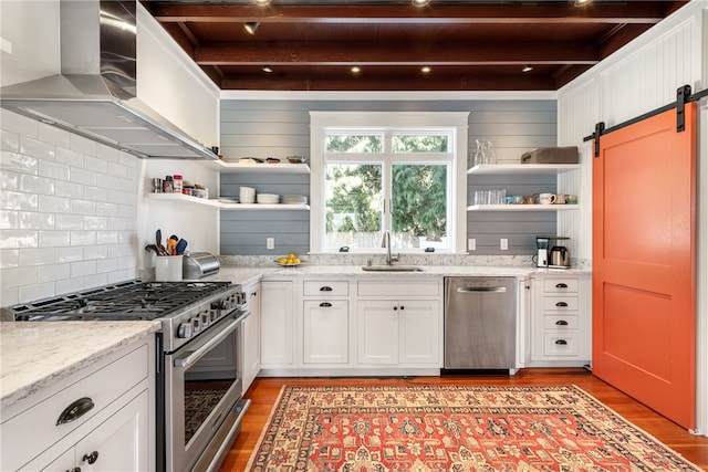 kitchen with open shelves, a sink, appliances with stainless steel finishes, a barn door, and wall chimney range hood