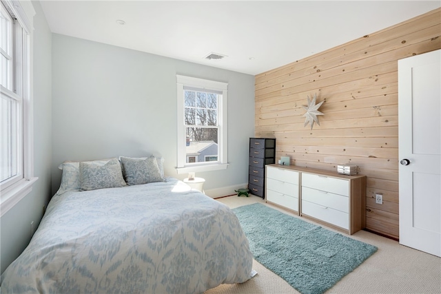 bedroom with wooden walls, visible vents, and light carpet