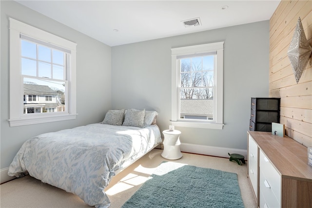 bedroom with visible vents, light carpet, baseboards, and wood walls