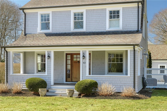 view of front of property featuring covered porch, a front yard, roof with shingles, and fence