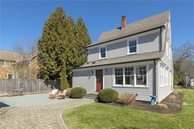 view of front facade featuring a patio, fence, a front yard, a shingled roof, and a chimney