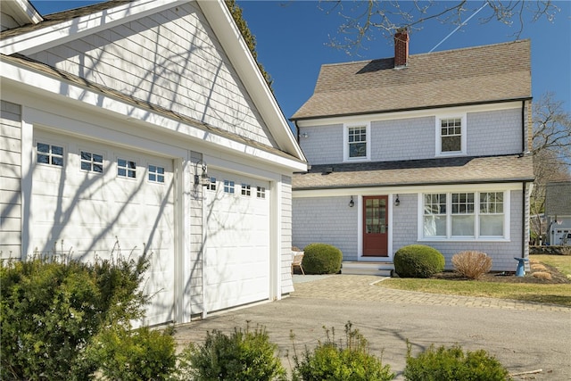 view of front of property featuring a chimney, driveway, and a shingled roof