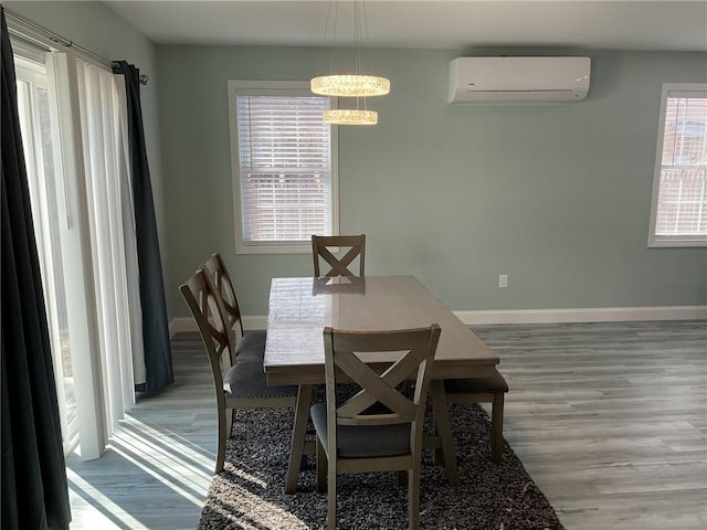 dining area with a notable chandelier, wood finished floors, baseboards, and a wall mounted AC