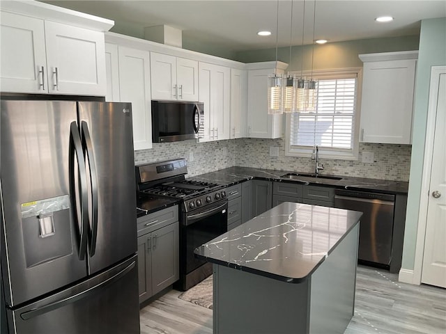 kitchen with light wood-style flooring, a sink, decorative backsplash, stainless steel appliances, and decorative light fixtures