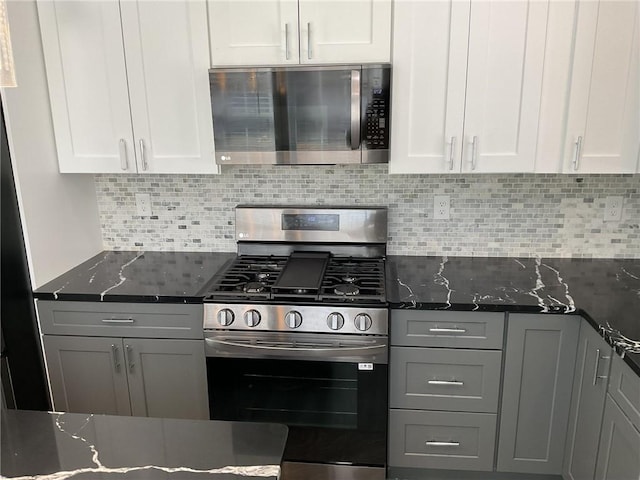 kitchen with gray cabinets, white cabinetry, dark stone counters, appliances with stainless steel finishes, and decorative backsplash