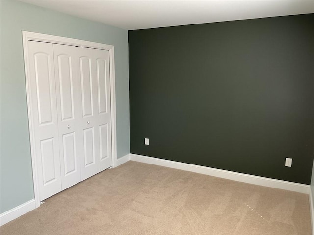 unfurnished bedroom featuring baseboards, a closet, and light carpet