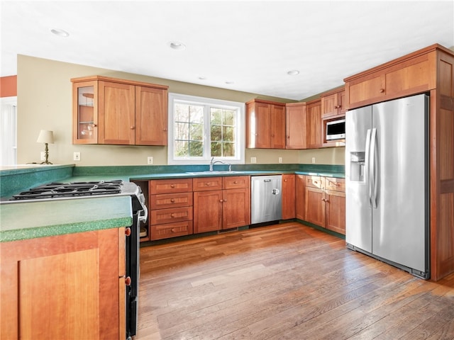 kitchen featuring recessed lighting, light wood-style flooring, brown cabinets, stainless steel appliances, and a sink