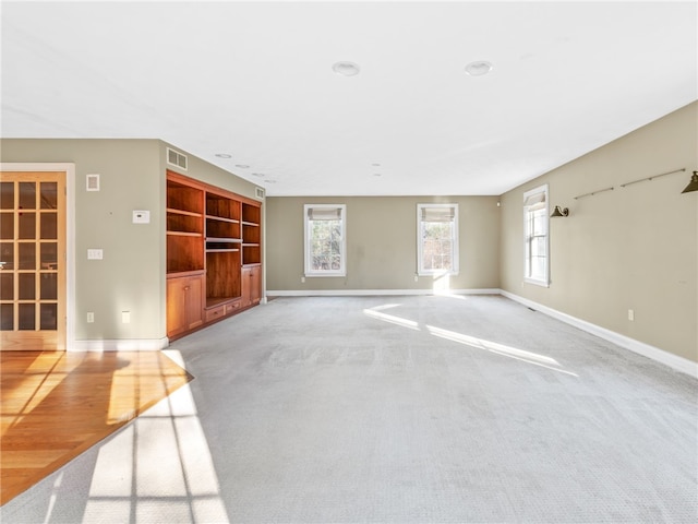 unfurnished living room with visible vents, baseboards, and light colored carpet