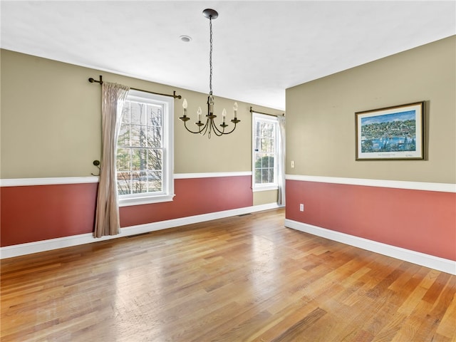 spare room with an inviting chandelier, wood finished floors, and baseboards