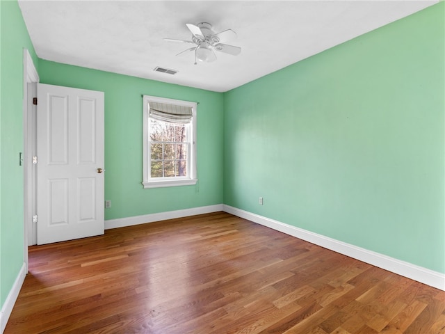 unfurnished room featuring baseboards, wood finished floors, visible vents, and ceiling fan