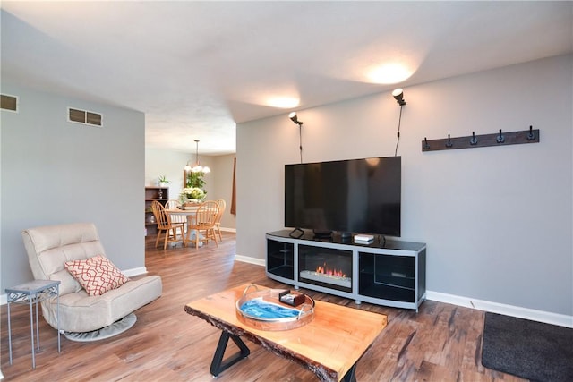 living room with an inviting chandelier, wood finished floors, visible vents, and baseboards