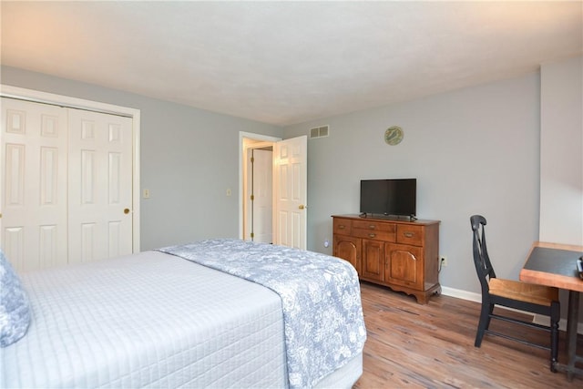 bedroom with light wood-type flooring, visible vents, baseboards, and a closet