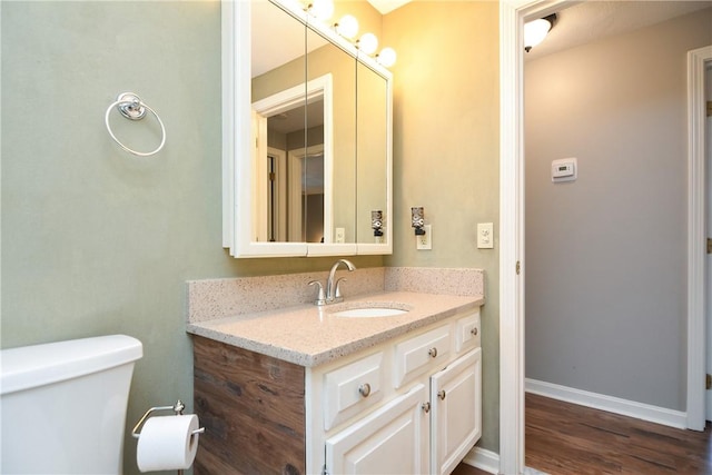 bathroom with vanity, toilet, wood finished floors, and baseboards