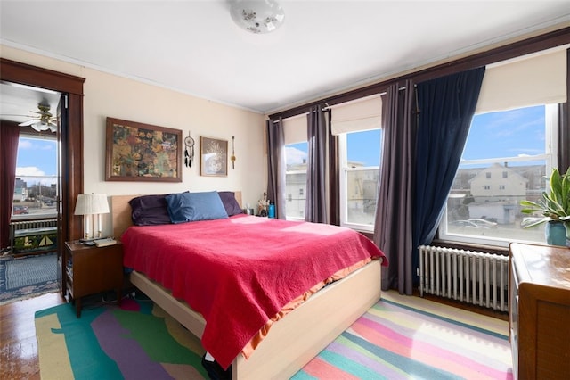 bedroom with multiple windows, radiator heating unit, and wood finished floors