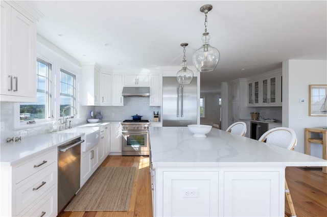 kitchen featuring a center island, under cabinet range hood, a breakfast bar area, high end appliances, and a sink