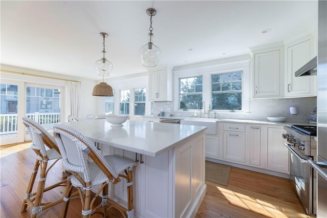 kitchen featuring a kitchen island, under cabinet range hood, light countertops, high end range, and a sink