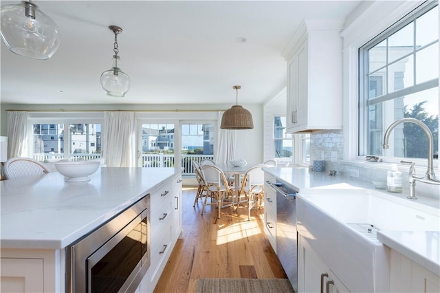 kitchen featuring a sink, stainless steel appliances, white cabinets, light wood-type flooring, and backsplash