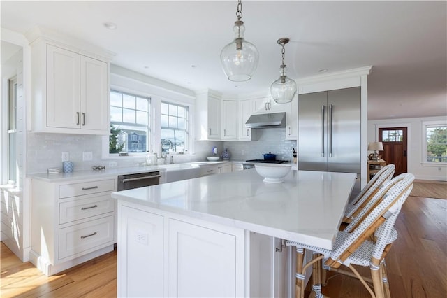 kitchen with light wood-style flooring, under cabinet range hood, a center island, white cabinetry, and stainless steel appliances