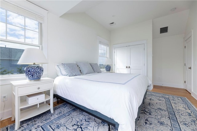 bedroom with visible vents, multiple windows, wood finished floors, and vaulted ceiling