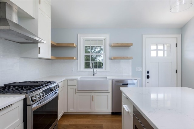 kitchen with open shelves, wall chimney range hood, appliances with stainless steel finishes, and a sink