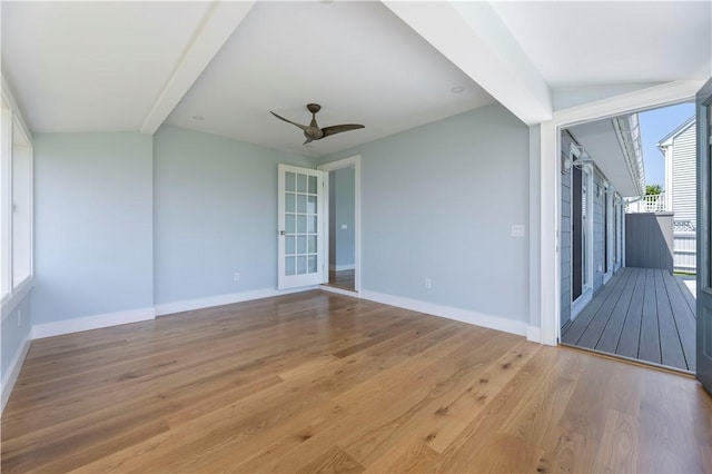 spare room featuring lofted ceiling with beams, baseboards, wood finished floors, and a ceiling fan