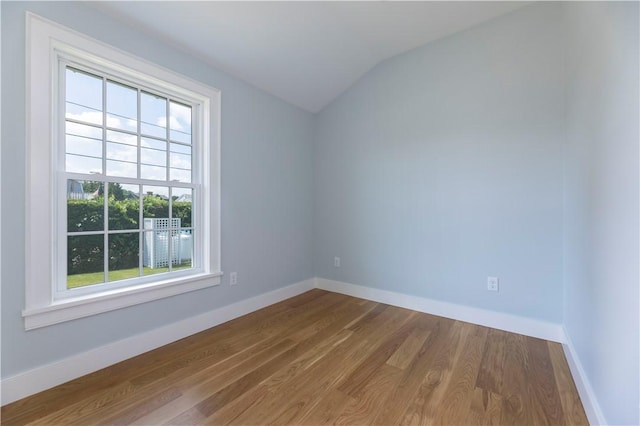 spare room featuring lofted ceiling, baseboards, and wood finished floors