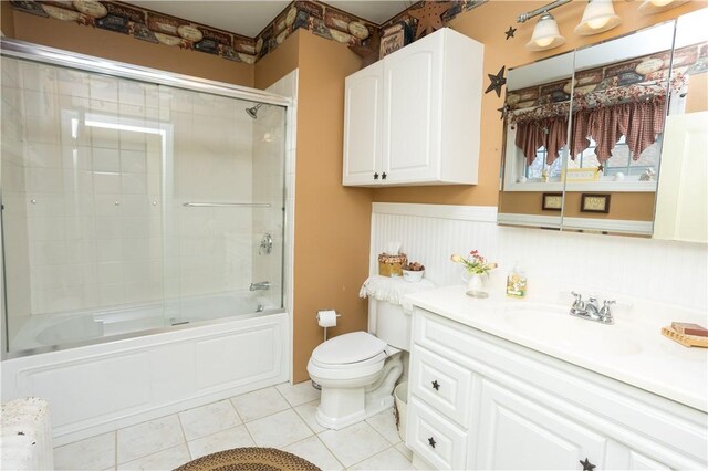 full bath with vanity, a wainscoted wall, bath / shower combo with glass door, tile patterned flooring, and toilet