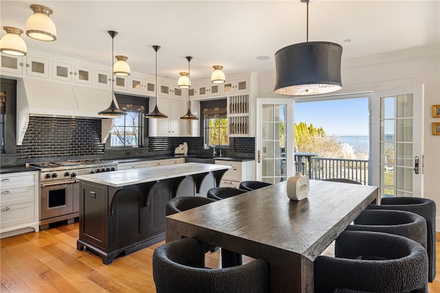 kitchen with high end stainless steel range, light wood-style flooring, decorative backsplash, and white cabinetry