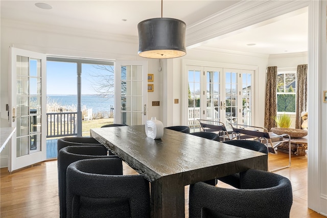 dining area with light wood finished floors, french doors, a water view, and crown molding