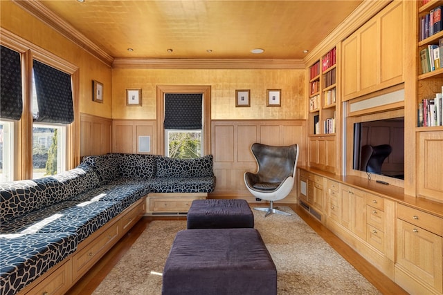living area featuring wood finished floors, built in shelves, ornamental molding, and wainscoting