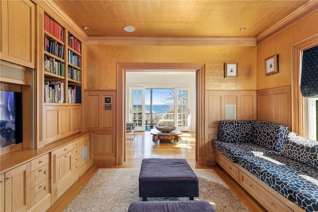 living room with light wood finished floors, wainscoting, built in shelves, and crown molding