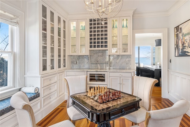bar featuring a healthy amount of sunlight, light wood finished floors, a chandelier, and wine cooler