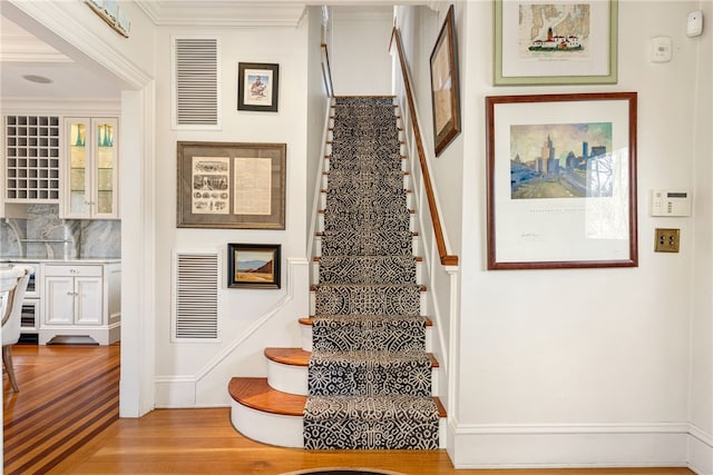 staircase featuring baseboards, wood finished floors, visible vents, and crown molding
