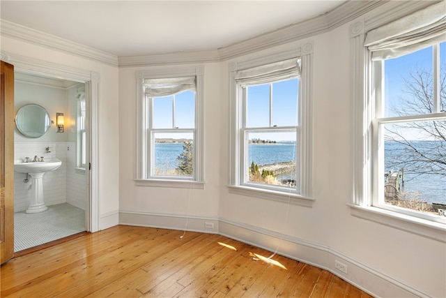 unfurnished bedroom featuring crown molding, ensuite bathroom, a water view, and light wood-type flooring