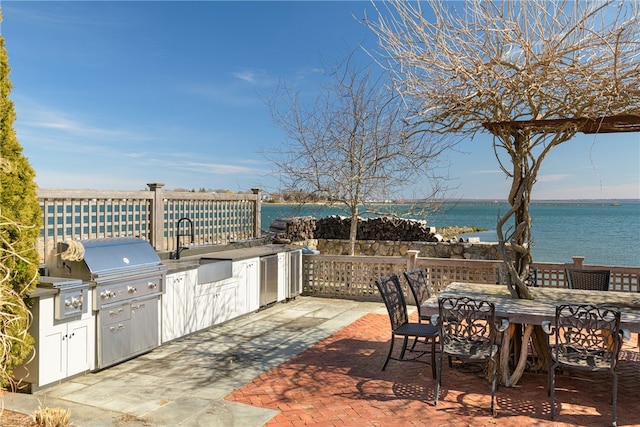 view of patio featuring grilling area, an outdoor kitchen, outdoor dining area, and a water view