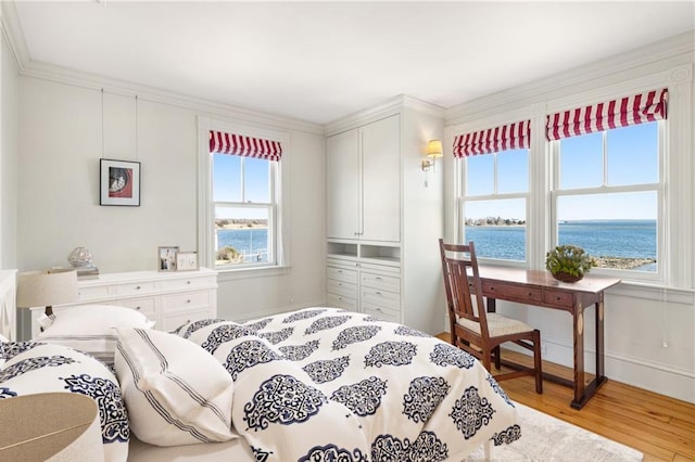 bedroom featuring baseboards, crown molding, light wood-style floors, and a water view
