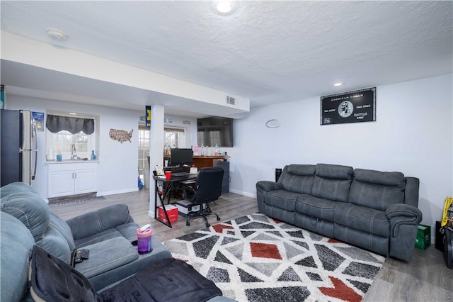 living room with wood finished floors, a textured ceiling, baseboards, and visible vents