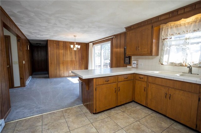 kitchen featuring brown cabinetry, an inviting chandelier, a sink, wood walls, and light colored carpet