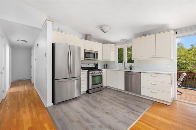 kitchen with light wood-style flooring, a sink, appliances with stainless steel finishes, light countertops, and lofted ceiling
