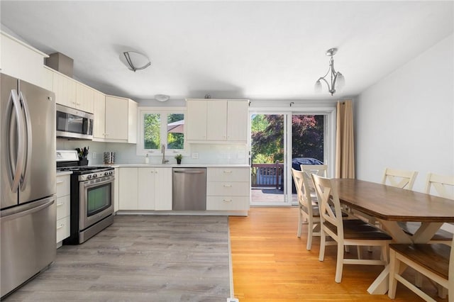 kitchen with light wood-style flooring, a sink, decorative backsplash, light countertops, and appliances with stainless steel finishes