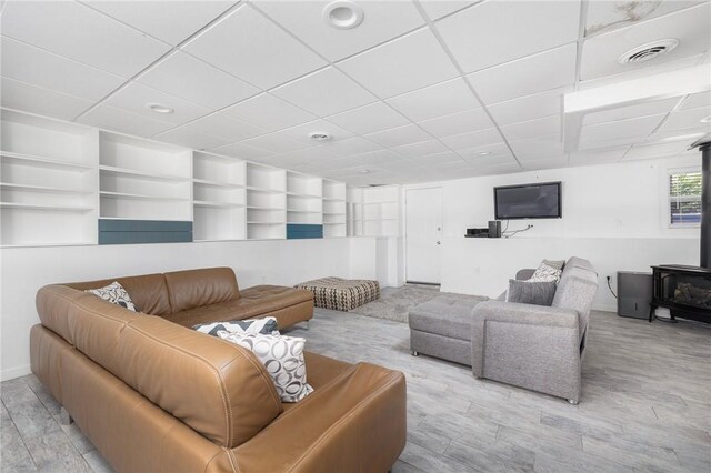 living area with a drop ceiling, visible vents, built in features, and a wood stove