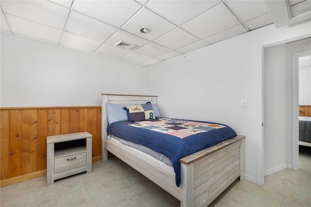 bedroom with a drop ceiling, visible vents, and wood walls