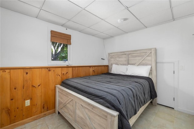 bedroom with light tile patterned floors, a drop ceiling, and wooden walls