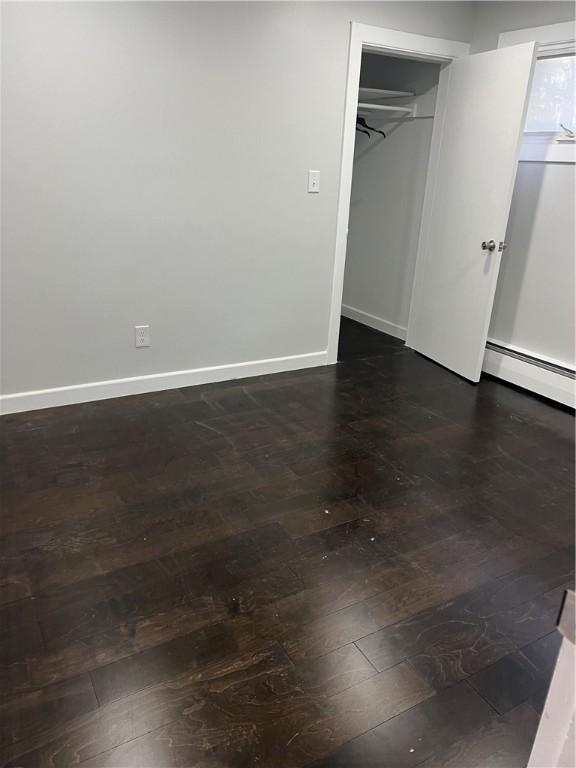 unfurnished bedroom with baseboards, a baseboard radiator, and dark wood finished floors