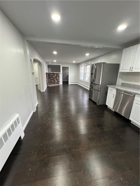 interior space with stainless steel appliances, arched walkways, white cabinetry, and radiator heating unit