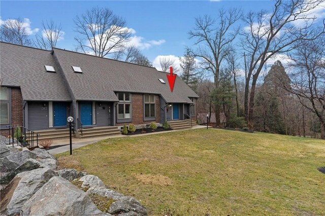 view of front of house with a shingled roof, a front lawn, and brick siding