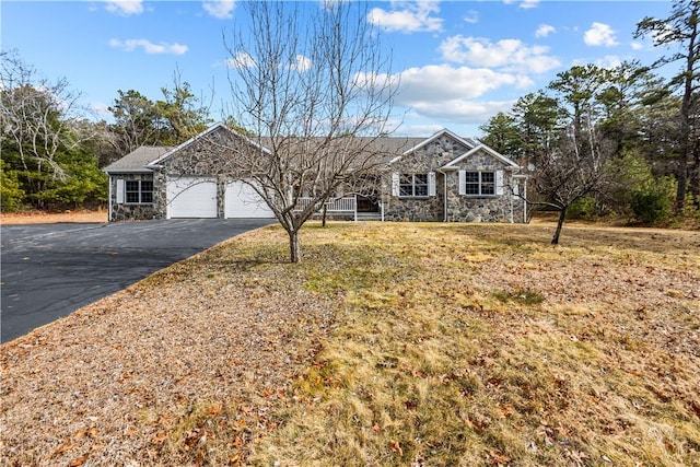 single story home with a front yard, a garage, stone siding, and driveway