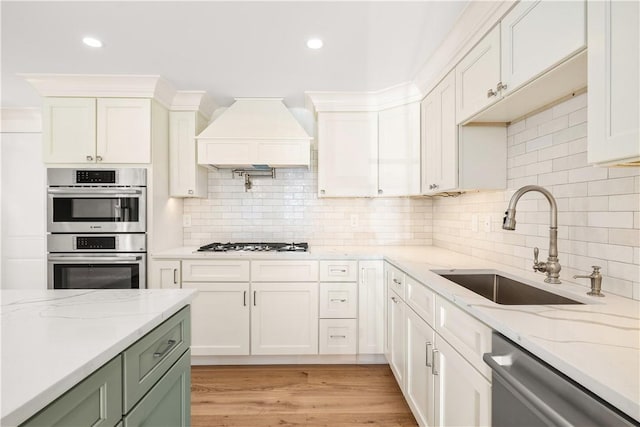 kitchen with light wood finished floors, a sink, custom range hood, white cabinets, and appliances with stainless steel finishes
