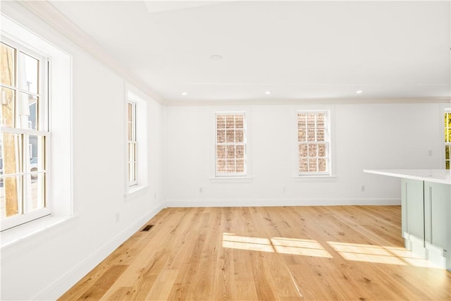 unfurnished room with visible vents, light wood-type flooring, baseboards, and ornamental molding