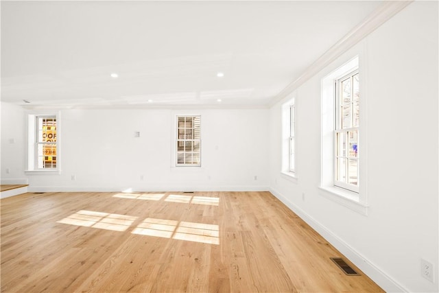 spare room featuring visible vents, baseboards, ornamental molding, and light wood finished floors